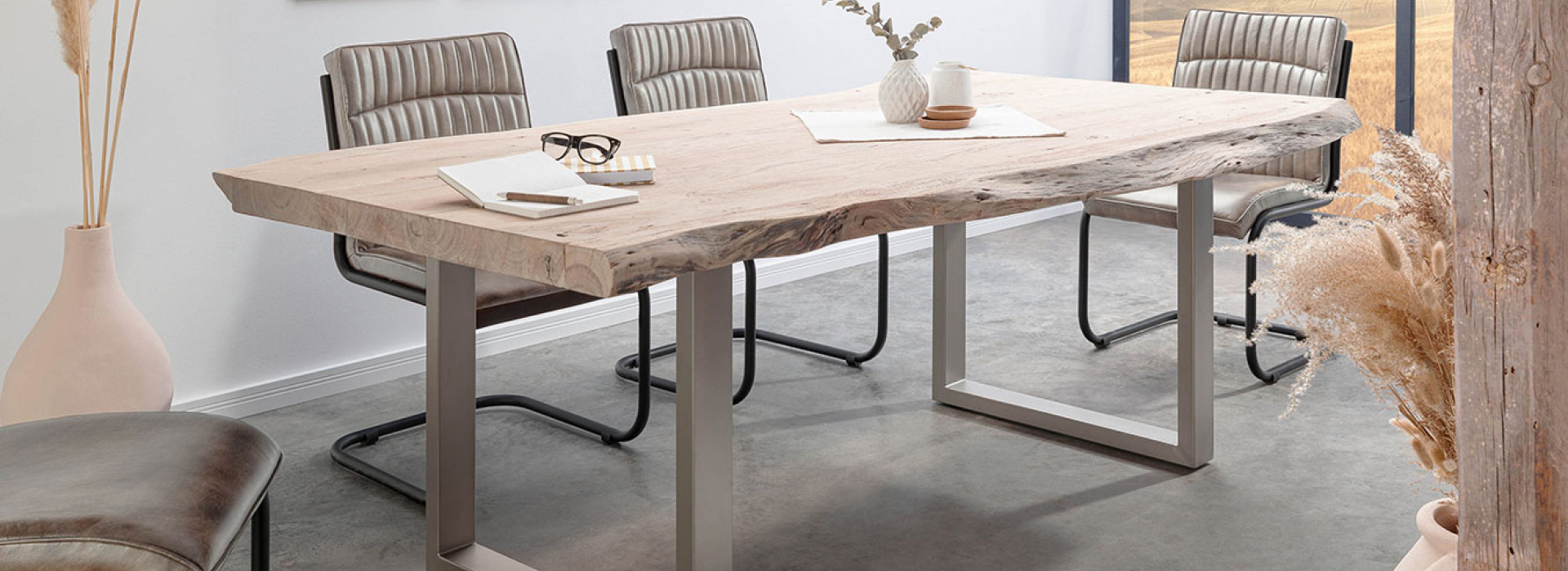 Boomtafel met massief houten blad en U-vormige poten in zilver, omringd door beige stoelen.