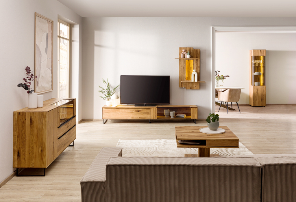 Lichte woonkamer met meubels van wild eiken, een tv-meubel, een dressoir en een warm verlichte wandplank als blikvanger.