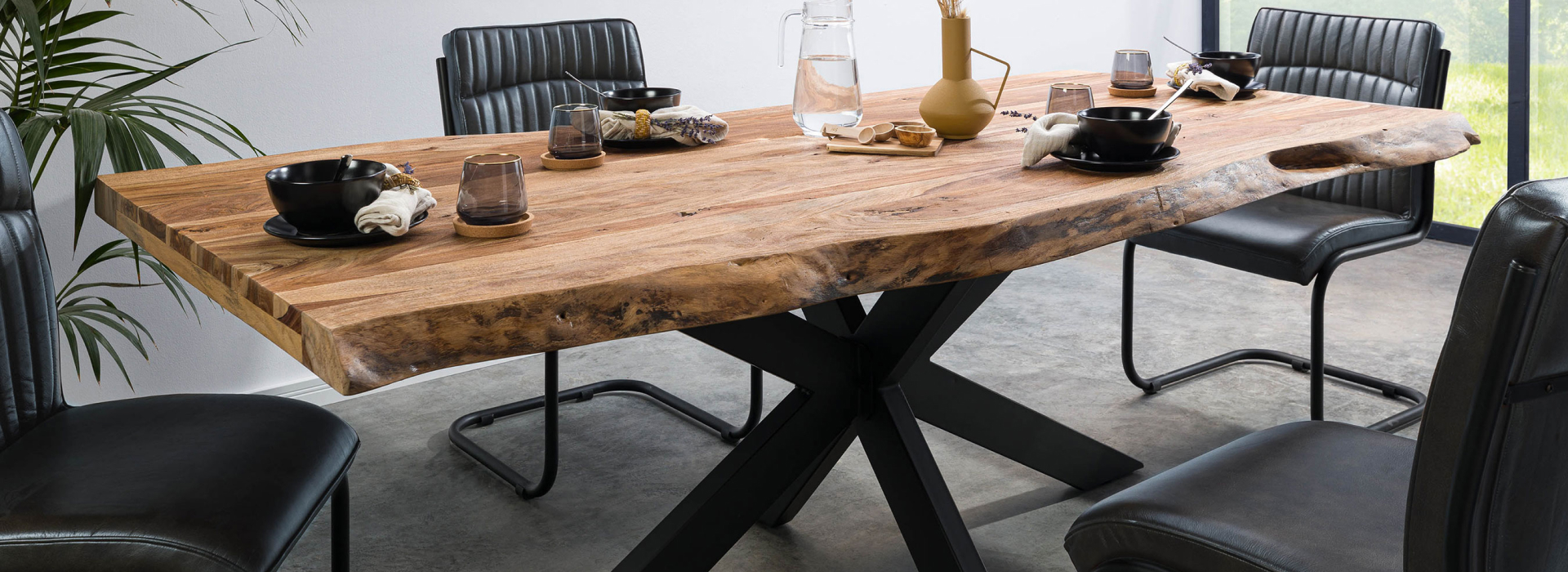 Boomtafel met massief houten blad en een kruisvormig onderstel in mat antraciet, omringd door bruine stoelen.