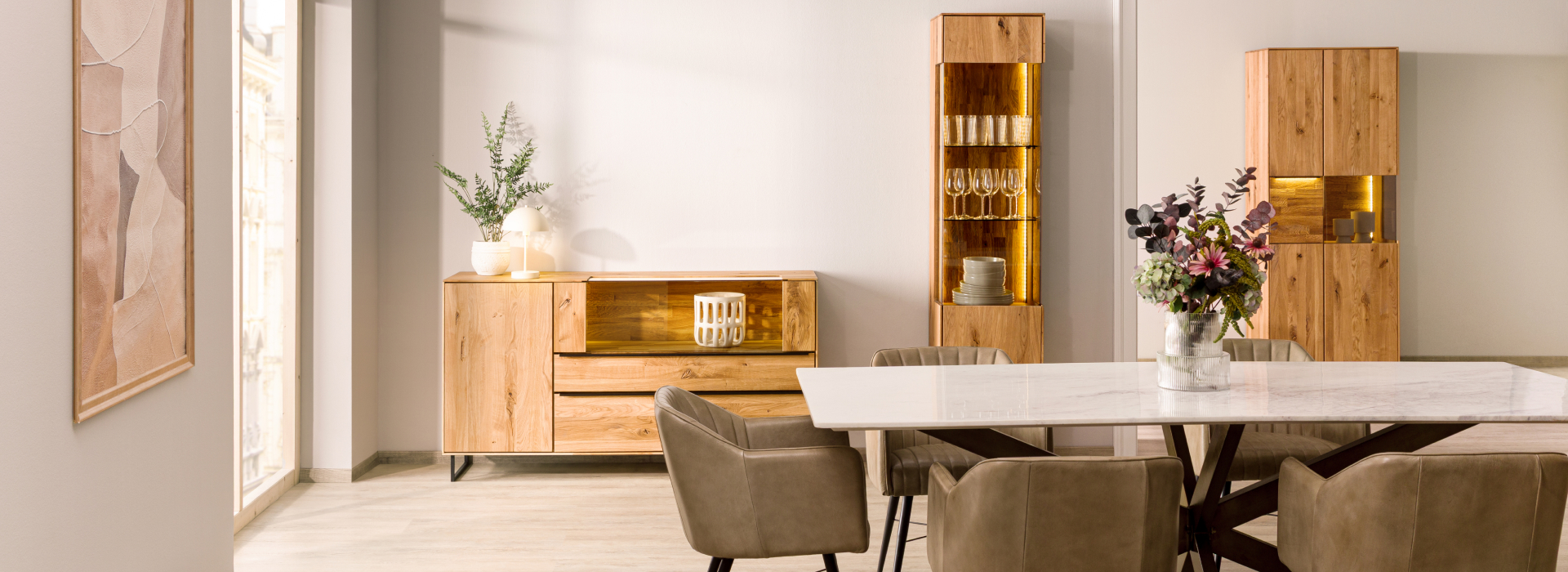 Lichte eethoek met wild eiken, verlichte vitrinekasten, een dressoir en een elegante eettafel met gestoffeerde stoelen.