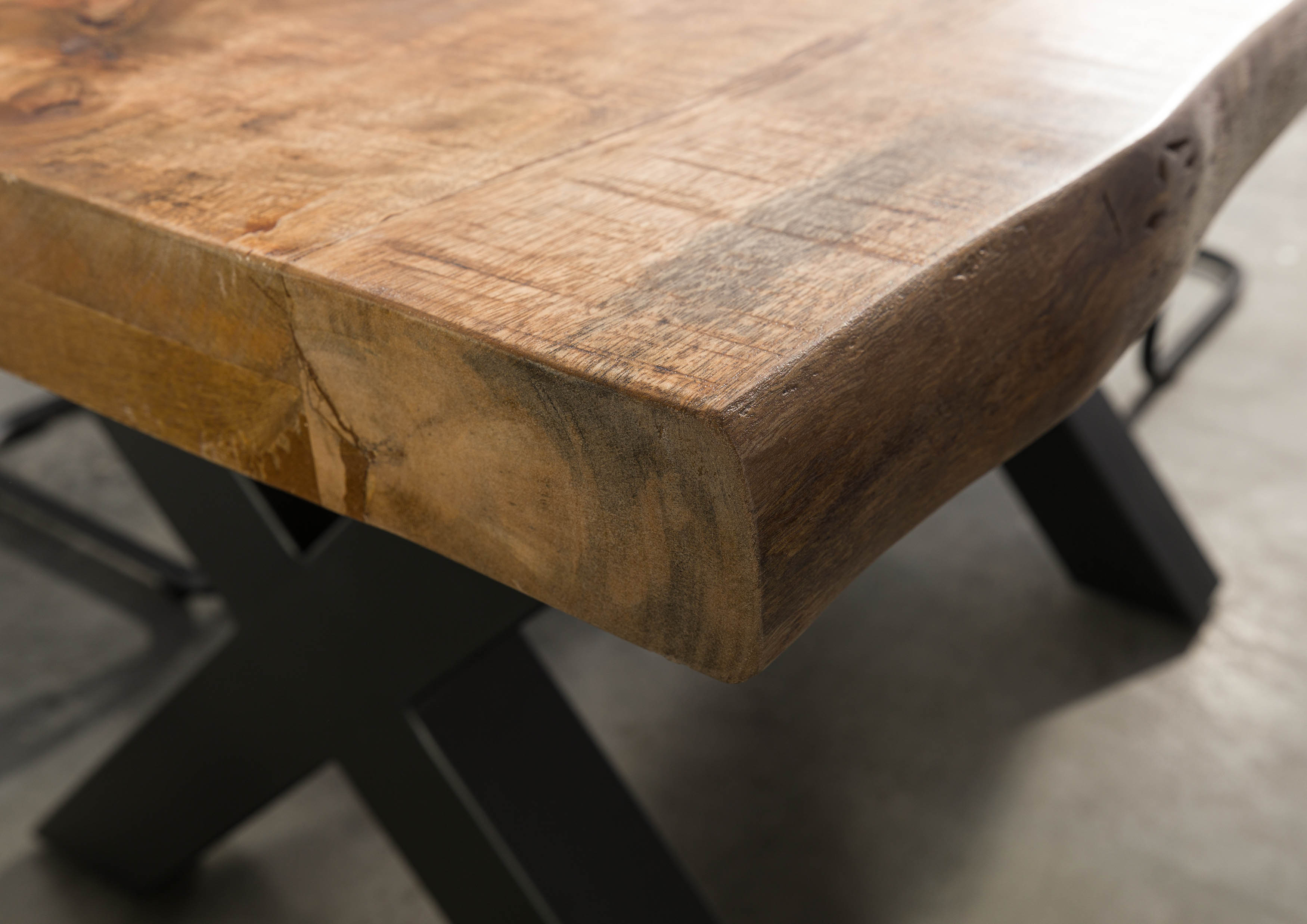 Detailfoto van een houten tafel met een natuurlijke houten rand en zwarte metalen poten in industriële stijl.